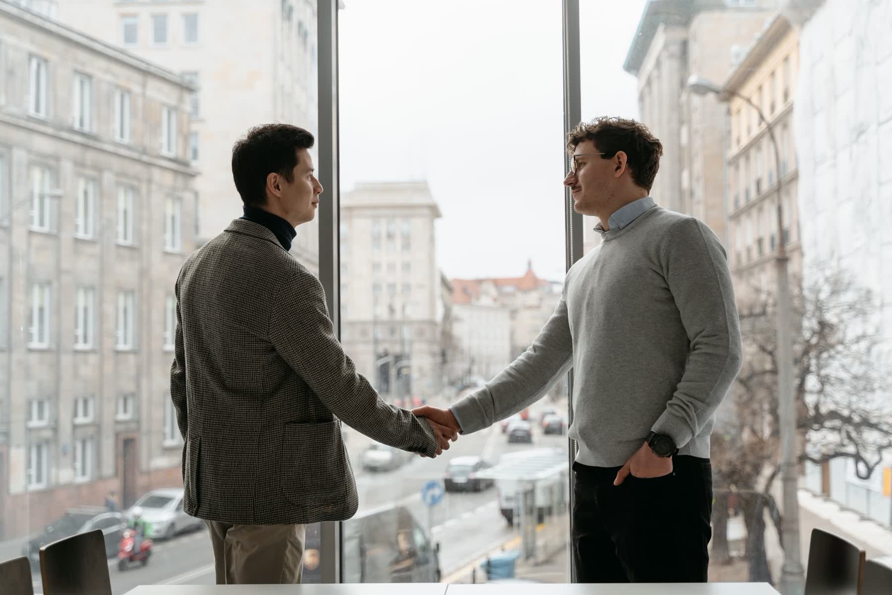 Dois executivos se cumprimentam com aperto de mão, com a cidade ao fundo